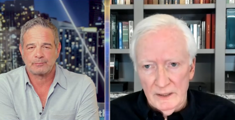 Split-screen video call: gray-haired man before a nighttime city skyline, white-haired man before a bookshelf