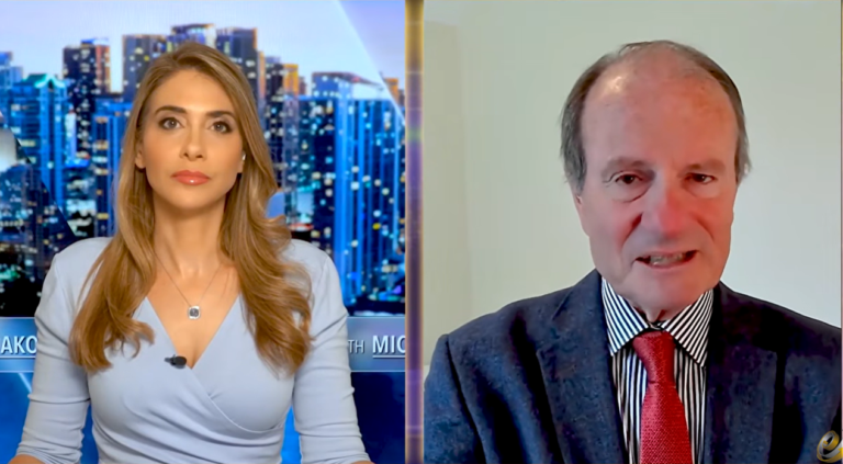 Split-screen interview: a woman sits before a city skyline while an older man in a suit and red tie speaks.
