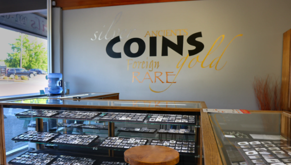 Coin shop interior with display cases of coins under a wall painted with 'COINS,' silver, gold and rare.