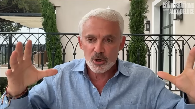 Gray-haired man with a goatee in a blue shirt gestures while speaking on a terrace; Gold Telegraph Conversations logo.