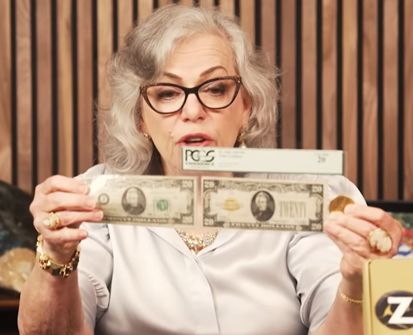 Gray-haired woman in glasses holding up two twenty-dollar bills sealed in plastic grading holders