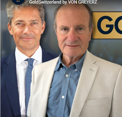 Two men in business attire pose before a 'GoldSwitzerland by VON GREYERZ' banner and gold-colored sign